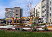 Thumbnail 4 of 65 - a courtyard with benches and a building with an flag  at Parks Residential - Richardson, Texas