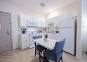 Thumbnail 17 of 65 - a kitchen with white cabinets and white appliances and a white table with two blue chairs at Parks Residential - Richardson, Texas, 75082