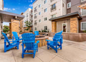Thumbnail 4 of 12 - a patio with blue chairs and a fire pit in front of an apartment building at Parks Residential - Denver, Centennial