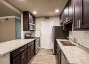 Thumbnail 4 of 16 - View into kitchen with stone counters, tile back splash, stainless appliances, and brown cabinets