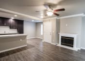 Thumbnail 6 of 16 - View from living room into kitchen and dining, with wood like flooring, ceiling fan, fireplace, view of bar countertop, tile backsplash, and brown cabinets