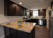 Thumbnail 20 of 27 - view of kitchen with stone counters, inlaid sink, well lit window above sink, brown cabinets, and stainless appliances