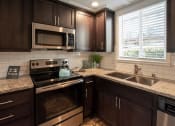 Thumbnail 19 of 27 - view of kitchen with stone counters, inlaid sink, well lit window above sink, brown cabinets, and stainless appliances