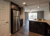 Thumbnail 17 of 27 - view from kitchen to living room wth wood look flooring, stainless appliances, tile backsplash, stone counters, ceiling fan, and private patio/balcony access via sliding glass door