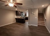 Thumbnail 15 of 27 - View from living and dining area into kitchen and up stairs in town homw, featuring wood look flooring, stone counters, tile backsplash, stainless appliances, brown cabinets, veiling fan and stairs leading upstairs
