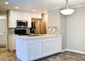 Thumbnail 13 of 25 - A kitchen with white cabinets and a wooden floor.