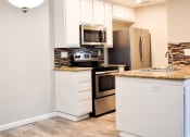 Thumbnail 24 of 25 - View of kitchen with stainless appliances, stone counters, tile backsplash, white cabinets and wood look flooring