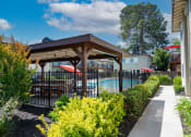 Thumbnail 19 of 34 - View into gated community pool with covered area that has a picnic table and seating areas, surrounded by lush landscaping