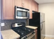 Thumbnail 7 of 34 - View of kitchen with stone counters, stainless appliances, tile backsplash, and brown cabinets