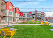 Thumbnail 54 of 76 - A grassy area with picnic tables and benches in front of apartment buildings.