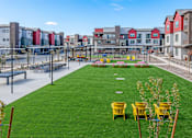 Thumbnail 52 of 76 - A grassy area with yellow chairs and a playground in the background.
