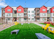 Thumbnail 53 of 76 - A grassy area in front of apartment buildings with yellow chairs and tables.