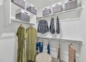 Thumbnail 11 of 54 - A white closet with clothes hanging and boxes on the shelf.