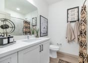 Thumbnail 26 of 54 - A bathroom with a white toilet, sink, and a framed picture on the wall.