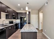 Thumbnail 4 of 24 - A kitchen with a granite countertop and dark wood cabinets. at The Premiere at Dana Park, Mesa