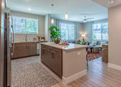 Thumbnail 17 of 52 - A kitchen with a refrigerator on the left and a dining area with a table and chairs.