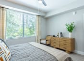 Thumbnail 10 of 52 - A bedroom with a bed, nightstand, and window with blinds.