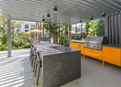 Thumbnail 30 of 52 - A grey concrete bench with a metal frame is in the foreground of a sunny outdoor area.