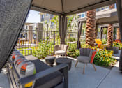 Thumbnail 5 of 52 - A patio with a grey sofa and a grey chair under a grey umbrella.