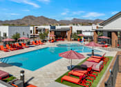 Thumbnail 1 of 35 - A pool surrounded by red chairs and umbrellas.at Marketside Villas at Verrado, Buckeye, AZ