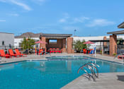 Thumbnail 2 of 35 - A swimming pool with red chairs and a building in the background.at Marketside Villas at Verrado, Buckeye, 85396