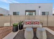 Thumbnail 24 of 35 - A modern outdoor living space with a white couch, two black planters, and a striped rug.at Marketside Villas at Verrado, Buckeye, AZ