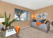 Thumbnail 18 of 36 - A living room with a grey couch, a wooden table, and a bicycle picture on the wall at Montage at Pecos Ranch Apartments, Arizona, 85286