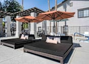 Thumbnail 26 of 40 - Two cushioned daybeds are placed under umbrellas on a patio. at Lazo Apartment Homes, Chandler, AZ  