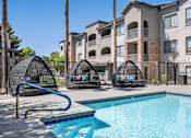 Thumbnail 23 of 40 - A swimming pool with a slide and two hanging chairs in front of apartment buildings. at Lazo Apartment Homes, Chandler, AZ 85225  