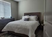 Thumbnail 4 of 14 - Bedroom with wooden furniture and white bedding at Pinon Lofts Apartments, Arizona