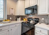 Thumbnail 5 of 42 - A black microwave is mounted above a black stove in a kitchen with white cabinets.at Palazzo Townhomes, Phoenix  