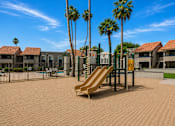 Thumbnail 18 of 20 - A playground with a slide, palm trees, and a swimming pool in the background.