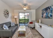 Thumbnail 4 of 34 - A living room with a grey couch, a white armchair, a coffee table, and a ceiling fan. at Reflections at Red Mountain Apartments, Mesa, AZ