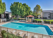 Thumbnail 2 of 34 - A swimming pool surrounded by a fence and trees at Reflections at Red Mountain Apartments, Mesa, Arizona