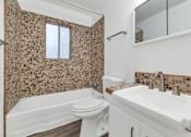 Thumbnail 14 of 26 - A bathroom with a brown tiled shower and a white sink at The Phoenix Apartments on 6th Avenue, Phoenix, Arizona