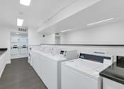 Thumbnail 26 of 36 - A row of white washing machines in a laundromat at Urban WalkApartments on 6th Avenue, Arizona