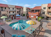 Thumbnail 34 of 36 - A pool surrounded by a fence and umbrellas in front of apartment buildings. at Urban WalkApartments on 6th Avenue, Phoenix, Arizona