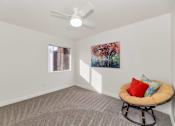 Thumbnail 7 of 36 - A room with a ceiling fan, a window, a carpeted floor, a chair with a cushion and a painting on the wall at Urban WalkApartments on 6th Avenue, Phoenix, Arizona