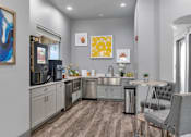 Thumbnail 23 of 29 - A modern kitchen with a grey chair and a table.