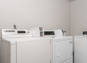 Thumbnail 5 of 8 - A row of white washing machines in a laundry room.