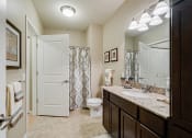 Thumbnail 10 of 25 - Bathroom with bright lights, brown cabinets, and light granite countertops