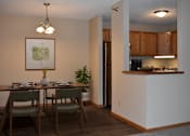 Thumbnail 4 of 32 - A dining room with a table set for two and a kitchen area in the background.