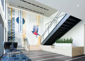 Thumbnail 5 of 44 - lobby with chairs, potted plants, and stairs against a mural of a bird and a sign that reads "Parker Station Flats"