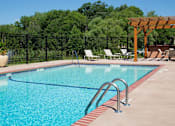 Thumbnail 15 of 32 - Outdoor pool surrounded by pool chairs and a fence, trees is the background