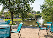 Thumbnail 24 of 32 - Outdoor patio with blue chairs, round tables, and a view of a lake with a fountain