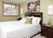 Thumbnail 11 of 32 - Bedroom with white comforter, decorative pillows, wooden headboard, and artwork of flowers hanging on the wall