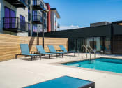 Thumbnail 16 of 44 - Pool and pool chairs next to apartment units' balconies and a blue sky