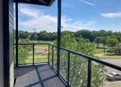 Thumbnail 26 of 44 - View from a unit's balcony, overlooking a street, a baseball diamond, and a green field with trees
