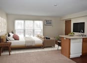 Thumbnail 12 of 32 - A bedroom with a bed, a couch, a chair, and a kitchenette.
