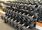 Thumbnail 11 of 76 - A rack of black dumbbells with white numbers ranging from 30 to 75.